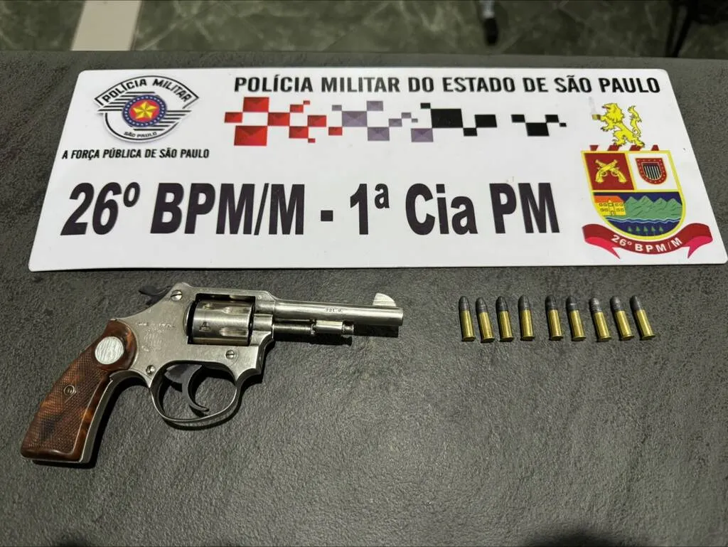 Foto de um revólver calibre 22 ao lado de nove munições, junto com uma placa do 26º Batalhão da Polícia Militar do Estado de São Paulo