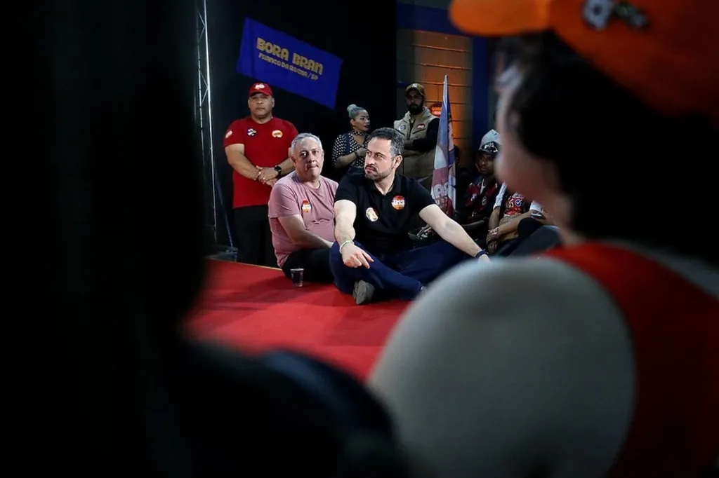 Bran e Kiko Celeguim sentados num palco durante plenária de campanha nas eleições de 2024