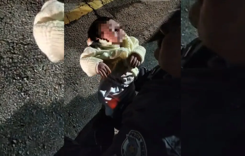 Policial com bebê recém-nascida nos braços após realizar uma manobra de desengasgo