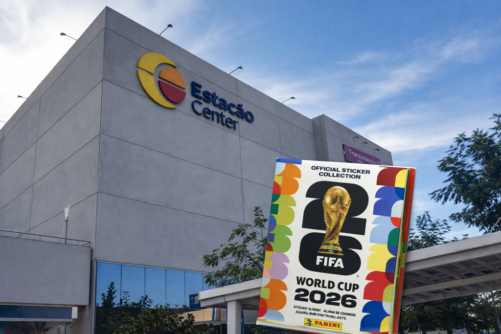 Fachada do Estação Center em Franco da Rocha, com o logotipo colorido visível na parte superior esquerda do prédio cinza. O céu azul e algumas árvores aparecem ao fundo. No canto inferior direito, em destaque, está o álbum oficial da Copa do Mundo FIFA 2026 da Panini, com design colorido e o troféu dourado centralizado entre os números “2” e “6”.